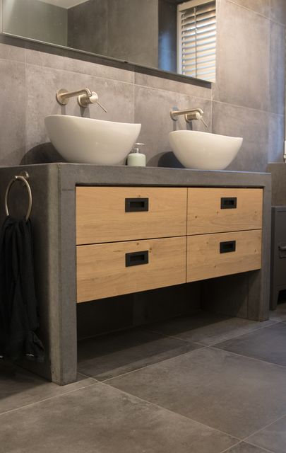 Badkamermeubel met houten laden, zwarte grepen, een donker frame en twee witte wastafels.