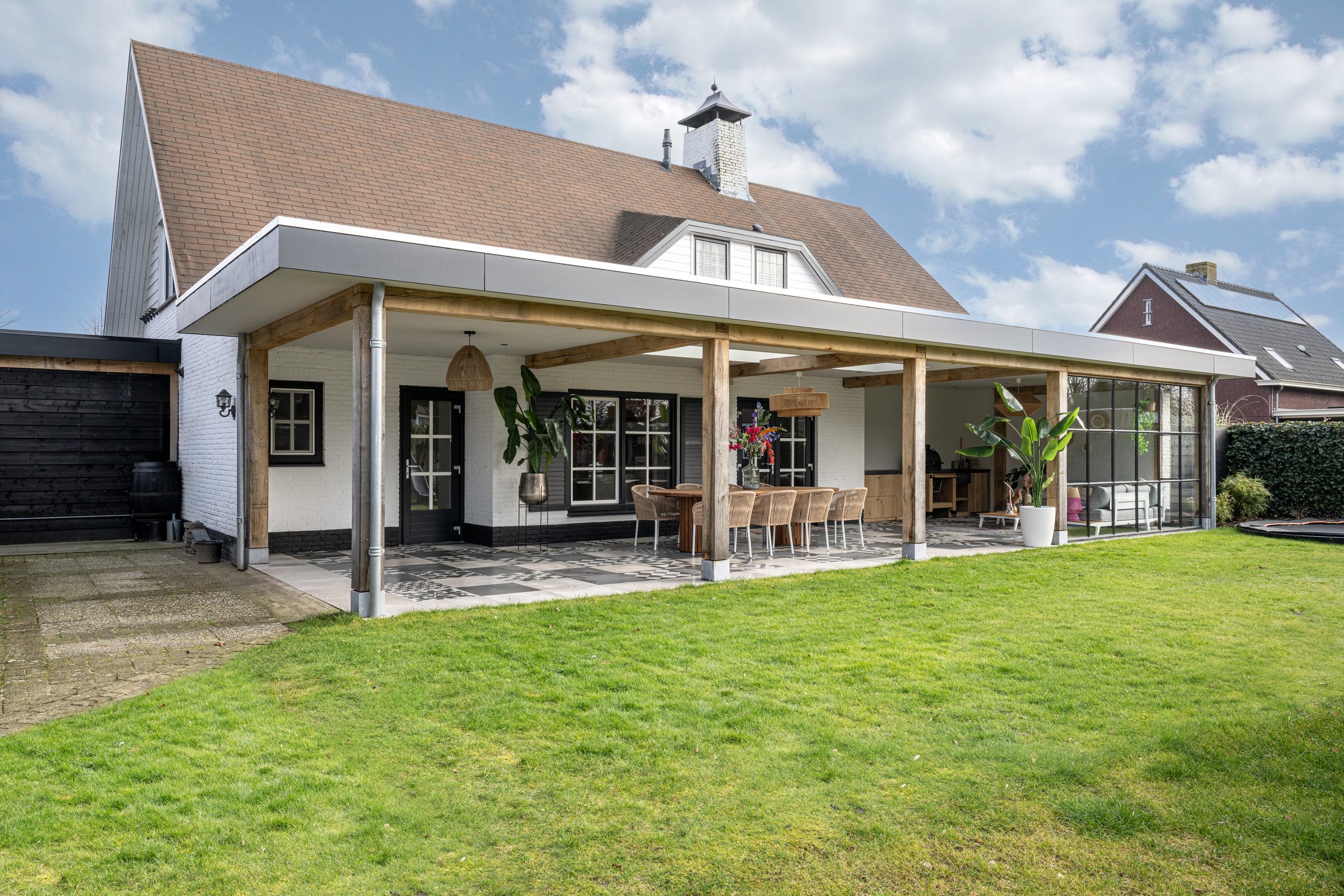 Overkapping aan een woning met staanders, glazen wanden en een terras naast het gazon.