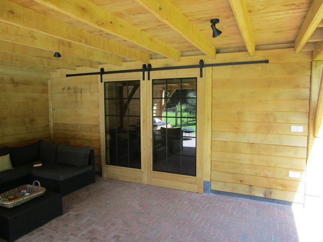 Twee houten schuifdeuren met glas en een zwarte bovenrail in een houten wand.