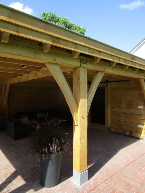 Houten staander met schuine schoren onder de dakconstructie van een overkapping.