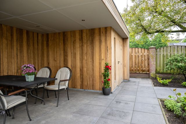 Terras onder een overkapping met plafondspots en verticale houten gevelbekleding.