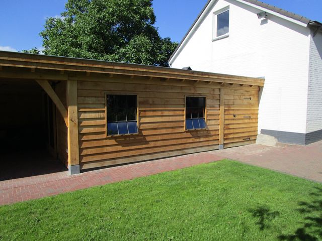 Houten gevel met twee ramen naast een open overkapping.