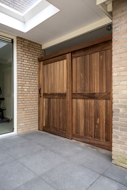 Houten deurpanelen onder een overkapping naast een bakstenen wand.