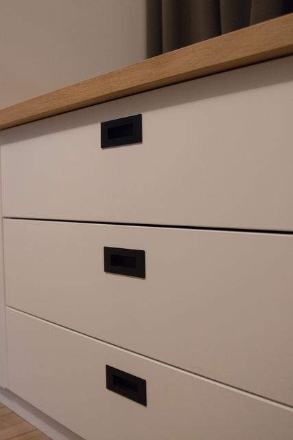 Witte ladefronten met zwarte komgrepen onder een houten blad.