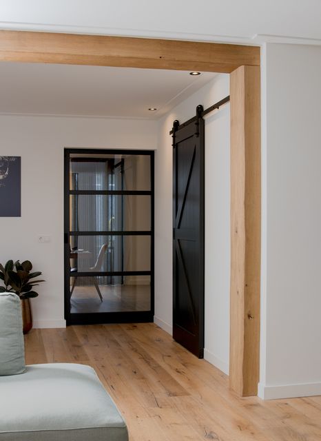 Doorkijk door een houten opening naar een zwarte glazen deur.