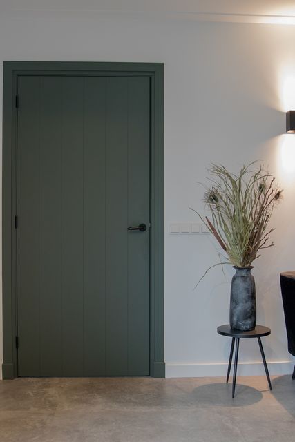 Grijsgroene paneeldeur in een witte wand boven een houten vloer.
