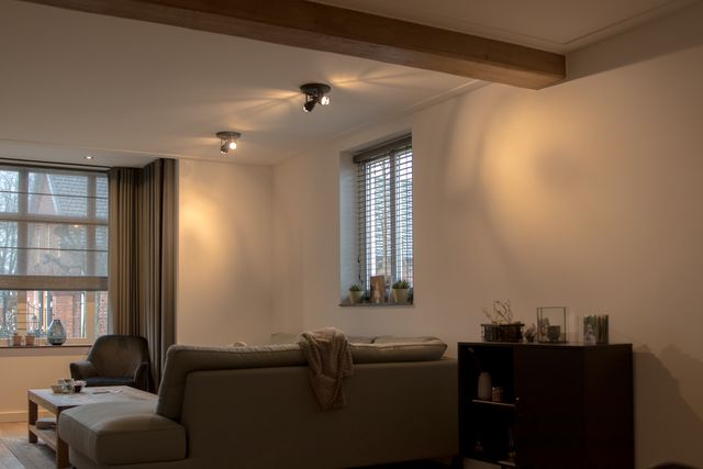 Woonkamer met zitmeubelen, ramen en gordijnen.