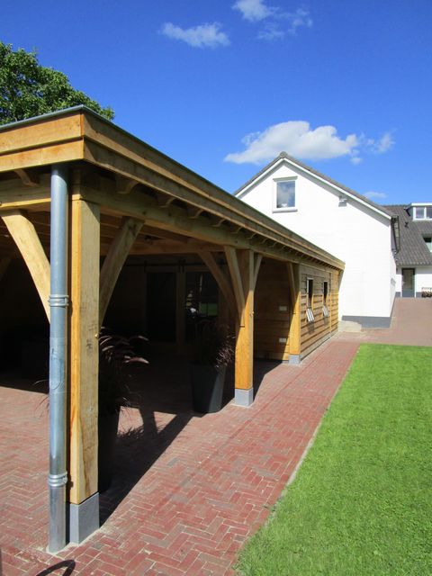 Zijaanzicht van een houten overkapping met staanders en terras.