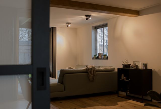 Doorkijk naar een woonkamer met zitmeubelen en ramen.