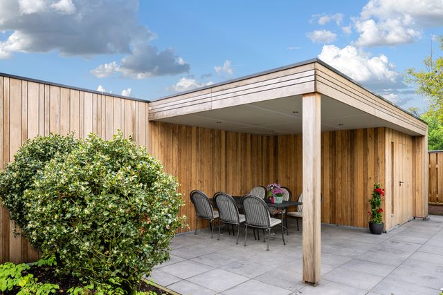 Zijaanzicht van een overkapping met verticale houten gevelbekleding en zitruimte.