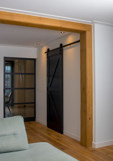 Donkere schuifdeur met glas, zwarte rail en een houten omlijsting.