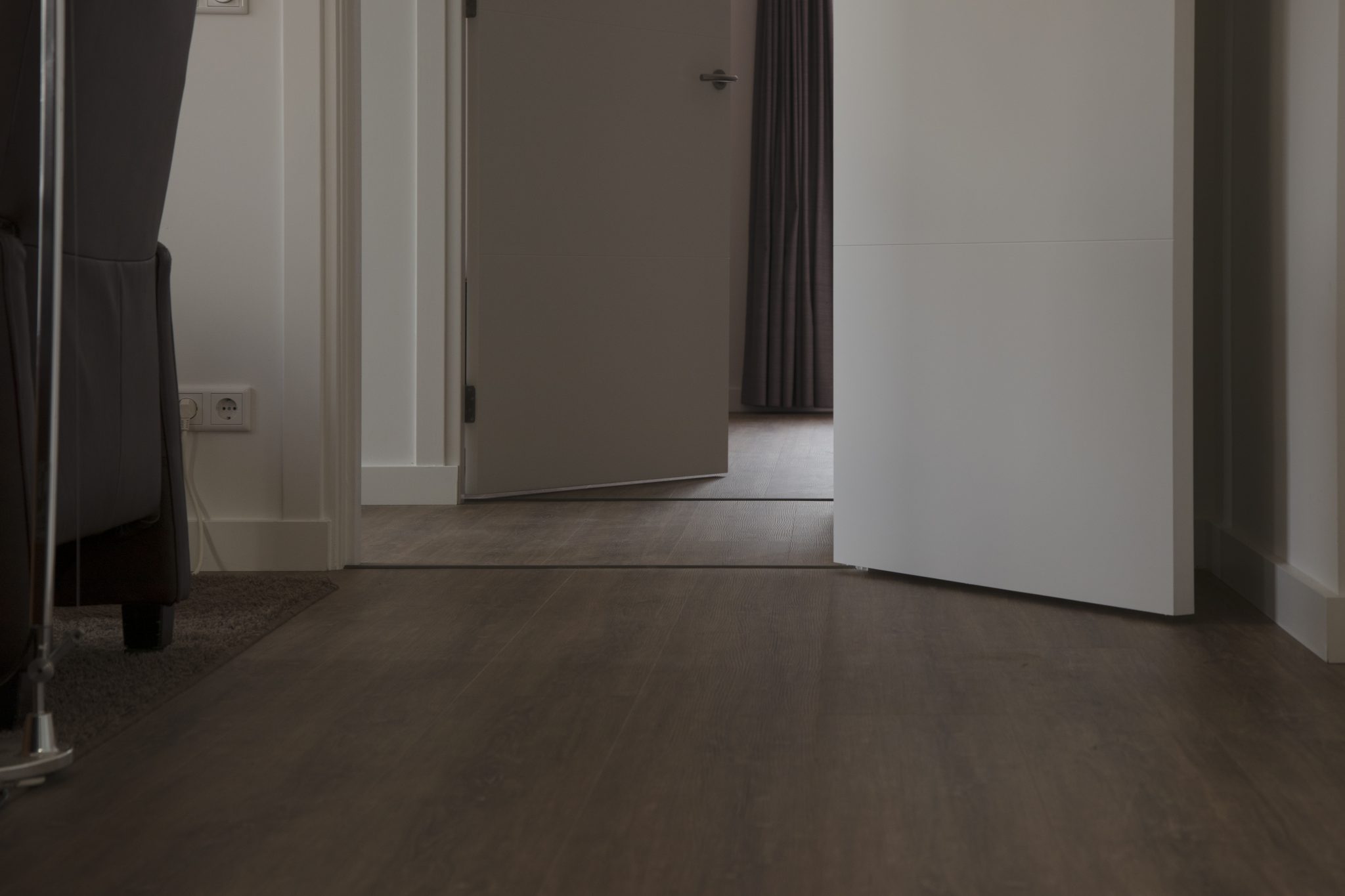 Donkere vloer met houtlook in een doorgang met lichte deuren en wanden.