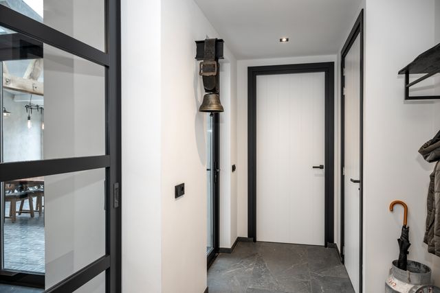 Zwarte glazen binnendeur naast een raam en een lichte wand.