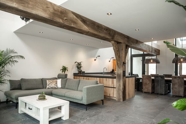 Open woonruimte met keuken, zithoek en zichtbare houten balken en staanders.