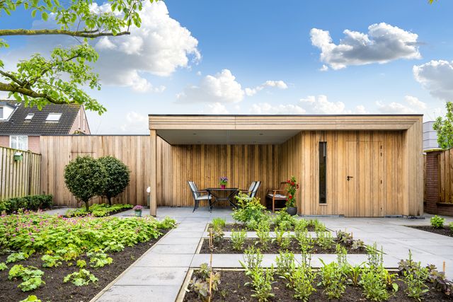 Tuin met overkapping, houten gevel en beplanting langs het terras.