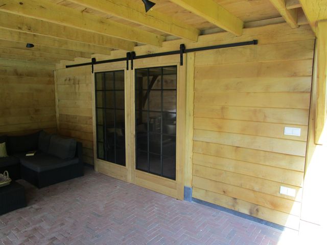 Houten schuifdeuren met glas en zwart hangwerk onder een overkapping.