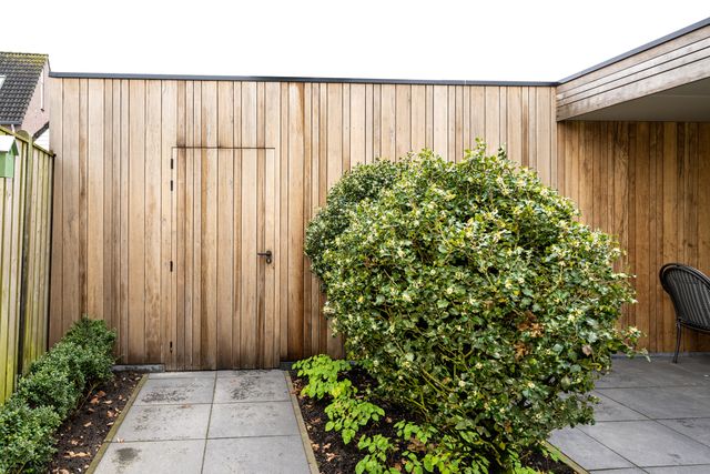 Verticale houten gevelbekleding met een deur opgenomen in hetzelfde wandvlak.